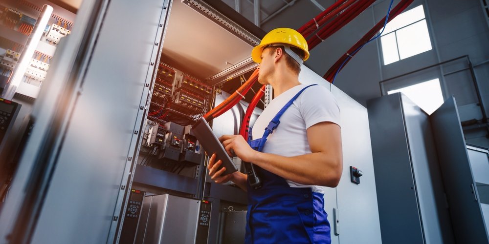 young,electrician,works,with,a,tablet,standing,near,an,industrial